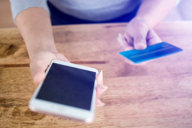 A person holding a credit card in their hand whilst using their mobile phone.